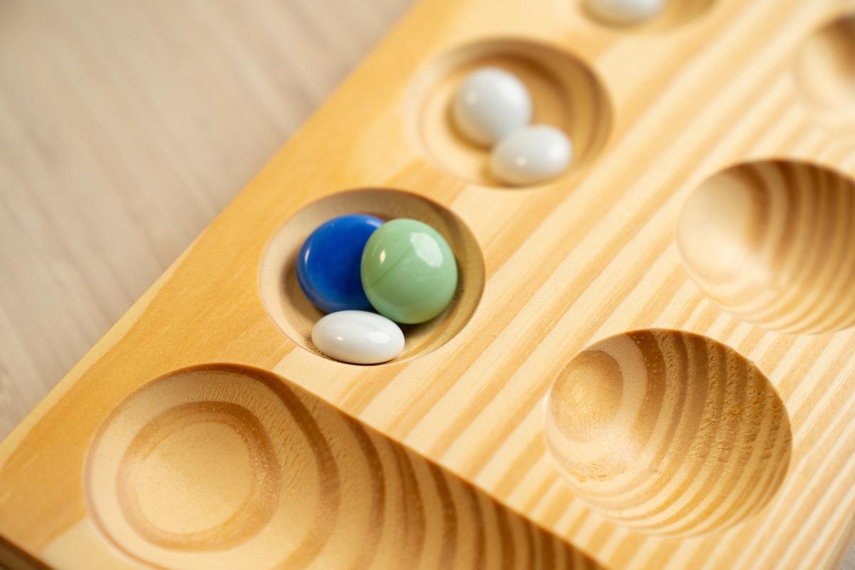 Mancala stones in pits on a Mancala board.